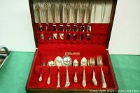 Complete flatware set displayed inside wooden box with red velvet lining, showing layout and quantity of various forks and spoons.