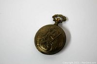 Closed view showing gold tone case with detailed hunter scene engraving featuring a bow and quiver.