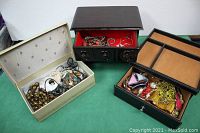 Three older jewelry boxes on green surface, each containing an assortment of necklaces and bracelets.
