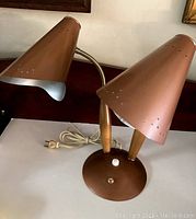 Full view of the desk lamp showing two brown metal cone shades on flexible gooseneck arms with wooden handles, mounted on a round metal base with control switches and power cord.