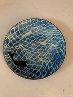 Top view of round enameled dish showing blue fish and fishing net pattern