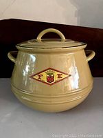 Yellow round enamel cast iron pot with lid and handles from FE Belgium showing front with logo.