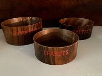 Three wooden snack bowls labeled Potato Chips, Peanuts, and Pretzels arranged on a table, showing exterior and interior condition.