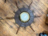 Full overhead view of Mid Century Modern wall clock showing round brass bezel, sunburst wooden elements, and metal decorative background with etched animal motifs on wooden floor.
