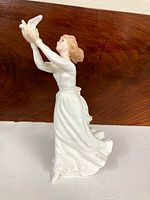 Right side view of the porcelain figurine showing the woman in a white dress holding two white doves aloft, with hair styled back.