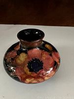 Front angle showing bulbous shape with peach, yellow, and dark blue floral motifs on black background.