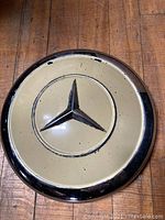 Top view of the full hubcap showing beige paint with wear and central Mercedes emblem.