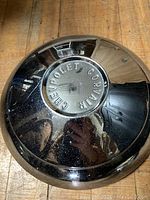 Front view of the Chevrolet Corvair hubcap showing embossed text and chrome finish with signs of wear.