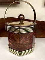 Front angle view of the octagonal vintage Kraftware ice bucket showing wood grain design, brass bands, hinged handle, and lid with knob.