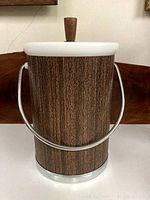 Front view of vintage Kromex ice bucket with woodgrain finish, white rim, and metal handle