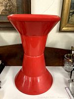 Front and side view of red molded utility stool with hourglass shape and flared base.
