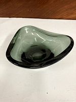 Side view showing the curved triangular shape and smooth finish of the dark green glass dish.