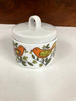 Photo of closed ceramic dish with bird design and lid on, showing side artwork and lid handle
