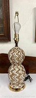Full view of table lamp showing the double-gourd shaped ceramic body with brown glossy finish and gold metallic pattern, brass socket, and gold colored base with electrical cord.