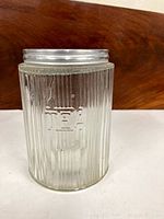Front view of clear ribbed glass tea canister showing embossed 'TEA' text and metal lid