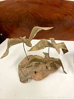 Front angle view of metal bird sculpture on burled wood base showing three birds in flight.