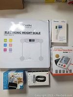 Boxed Triomph electronic weight scale, Berrcom thermometer, LTLKY blood pressure monitor, wrist blood pressure monitor, smart watch shown together