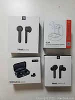 Four boxed wireless earbuds: SoundPEATS TrueBuds, TrueCapsule, TWS-Q8, and Enacfire G20, unopened and displayed on surface.