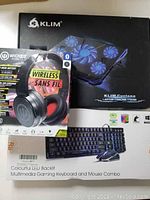 Lot packaging showing Klim Cyclone laptop cooling stand box, Wicked Audio wireless Bluetooth headphones box, and colorful LED backlit multimedia gaming keyboard and mouse combo package.