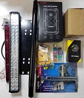 Photo showing FCONEGY car jump starter packaging, two LED light bars (one white, one red), black mounting bracket, fuse box, anti-theft device packaging and cables/connectors.