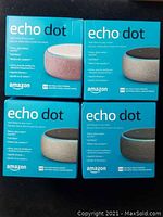 Four Amazon Echo Dot boxes in two grey, one black, one pink color variations, showing front product names and Alexa commands.