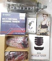 All items included in the workout lot packed together on a flat surface - jump rope, smart watch box, muscle toner, abdominal trainers, protein shakers, and water bottle.