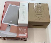 Photo showing boxed Fancii Gala vanity mirror, boxed facial rejuvenation device, and boxed facial steamer.
