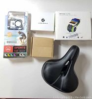 Top view of lot items arranged - bicycle seat, sports camera in packaging, Linpa World wireless earphones box, bicycle audio multifunctional speaker box, cardboard box (likely bicycle light)