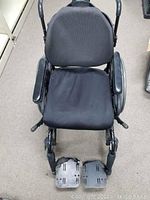 Full front view of the wheelchair showing padded black backrest, seat, and armrests with attached footrests.