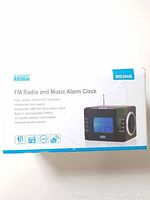 Box of August MB300B FM radio and music alarm clock with key features highlighted on packaging.