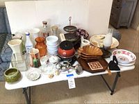 Full lot overview showing all items arranged on a white table including fondue pot, vintage bottles, ceramic bowls and decorative pieces