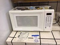 White GE microwave oven with digital keypad and display, placed on kitchen counter with manual in front