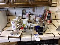Countertop view showing coffee mugs, cookbooks, salt and pepper shakers, pepper mill, and glass butter dish arranged on kitchen counter.