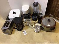 Overview of lot showing Rival electric skillet, Rival crock pot slow cooker, two coffee makers, blender, meat grinder, food processor, and toaster on floor