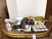 Overview of all baking pans and kitchen accessories arranged on a round wooden table including muffin tins, mixing bowls, vintage brass bowl with lid, glass dishes, and packaged grater/slicer.