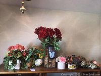 Silk flowers and foliage arranged in various ceramic pots, woven basket, and two stained glass tulip vases with blue and white tulip designs. Flowers are mostly red, pink, yellow silk, with some plastic flowers.