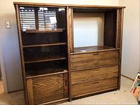 Front view of the wooden media center cabinet showing three drawers in the center, glass doors and shelves on the left, and a storage door below the glass.