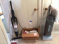 Photo showing Hoover upright vacuum and Oreck canister vacuum in a box with hose and attachments.