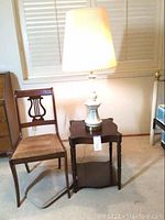 Photo showing ceramic table lamp lit on wooden side table next to harp back chair with brown corduroy upholstery
