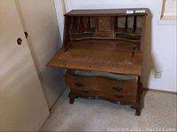 Photo showing the secretary dresser with the writing desk folded down, revealing multiple compartments inside and signs of wear on the writing surface.