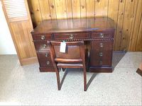 Front view of vintage wooden desk with attached wooden chair, showing multiple drawers and brass handles.