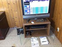 Sharp 32-inch TV on top of wooden media cabinet with glass doors, remote controllers and manuals on carpet in front.