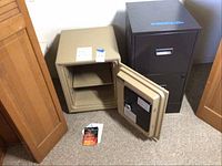 Open beige Saf-a-posit fire safe with electronic SAGA Screamer alarm, showing interior shelf and instruction manuals on floor beside it, next to closed brown metal file cabinet.