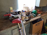 View of miscellaneous items on countertop including folding exercise bike with red seat, golf clubs, hardware, cords, tools, and green exercise ball.