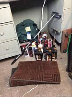 Photo showing seven bottles of Kendall 20W-50 motor oil, brown-striped floor mats folded in front, various car wash supplies on the floor, and a green coverall behind the items.