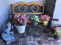 Full view of setup including wood and metal bench, bike planter holding four pots with silk flowers, and concrete welcome figurine of boy and turtle.