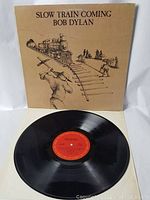 Vinyl LP record with red and orange center label, displayed in front of album cover. Record appears with scattered light surface wear.