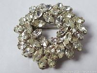 Front view showing circular brooch pin with clear crystals set in silver-tone metal.