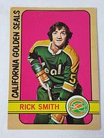 Front side of the 1972-73 OPC Rick Smith hockey card showing player in California Golden Seals jersey with pink background.