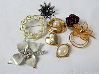 Eight vintage pins and brooches arrayed on a white surface showing the variety of styles and materials including metal, enamel and faux pearls.